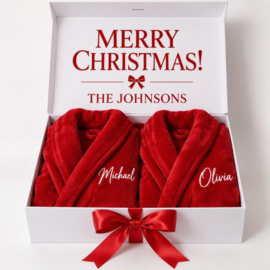 A white gift box containing two red robes with the names "Michael" and "Olivia" printed on them. The box is decorated with a red ribbon bow.