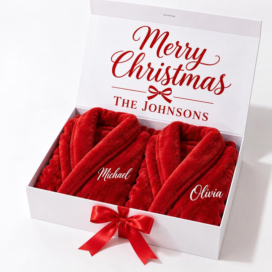 A white gift box containing two red robes with the names "Michael" and "Olivia" printed on them. The box is decorated with a red ribbon bow.